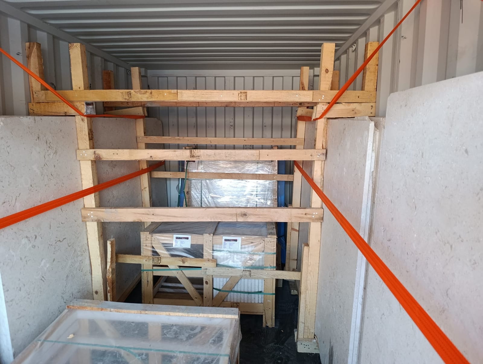 Inside a shipping container: stone slabs and wrapped crates braced with timber frames and orange straps