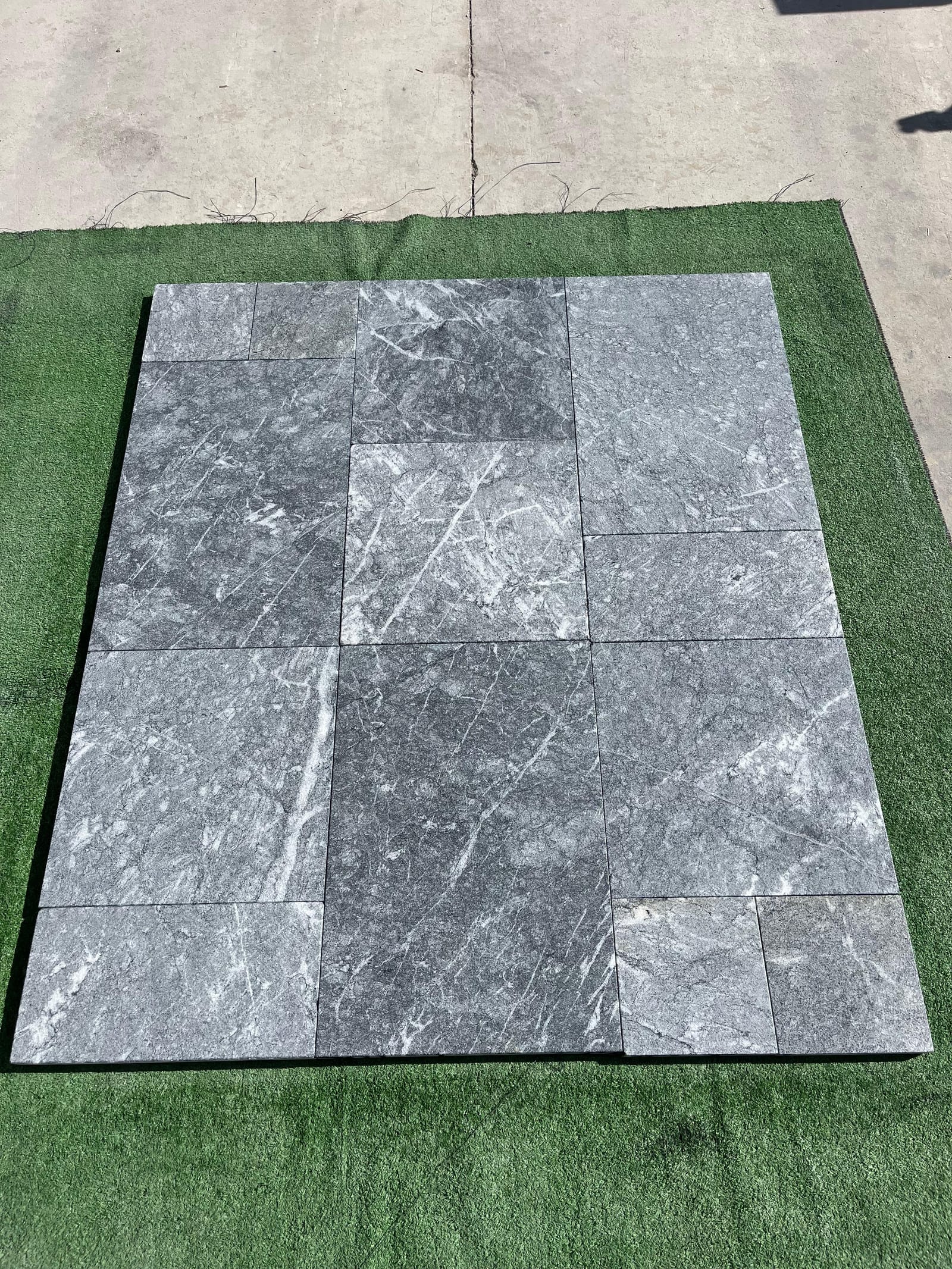 Grey marble pavers with white veining laid out in a pattern on artificial turf